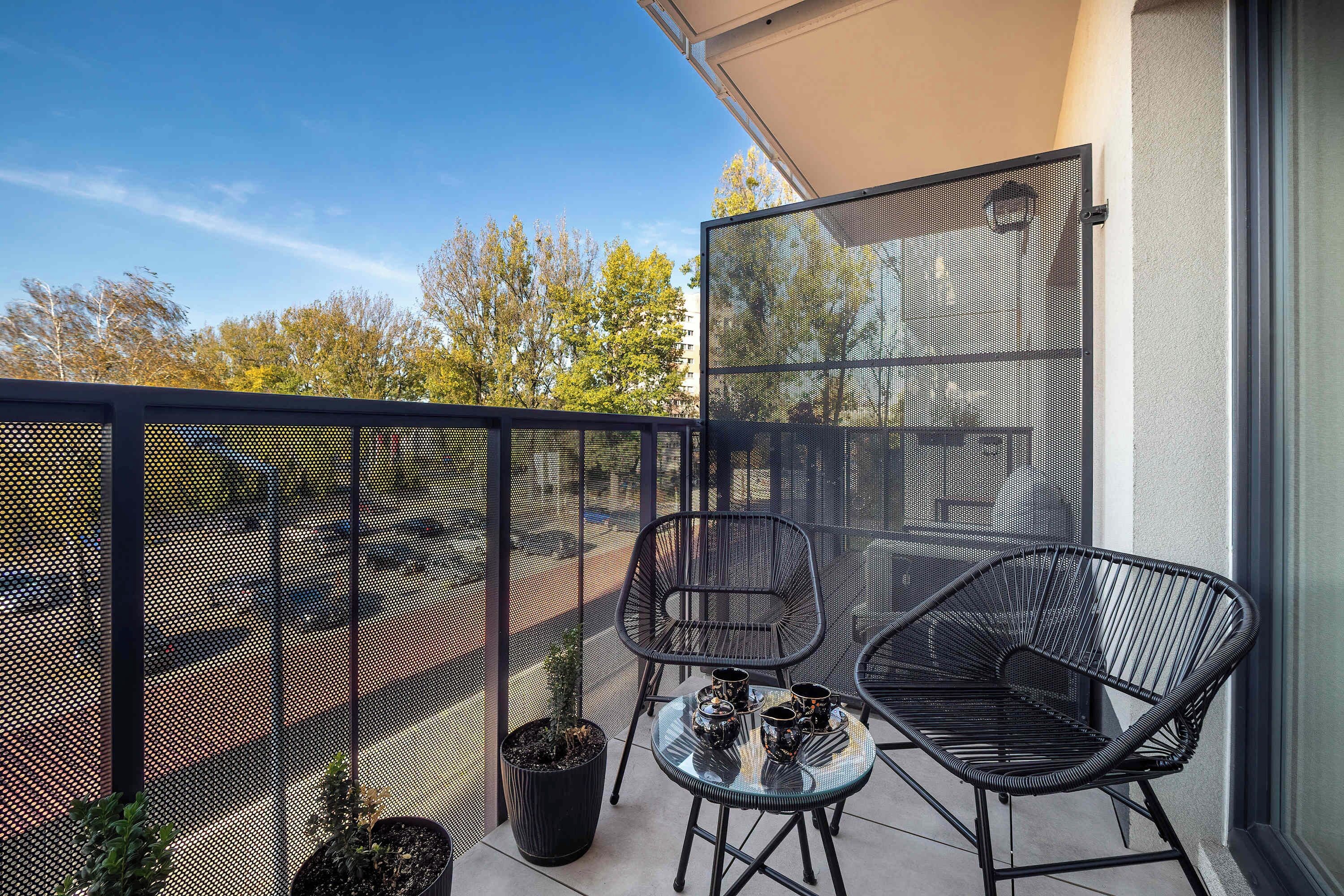 Een balkon met een gaashek, twee stoelen, een bijzettafeltje en een bloempot.