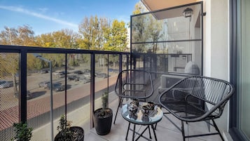 Een balkon met een gaashek, twee stoelen, een bijzettafeltje en een bloempot.