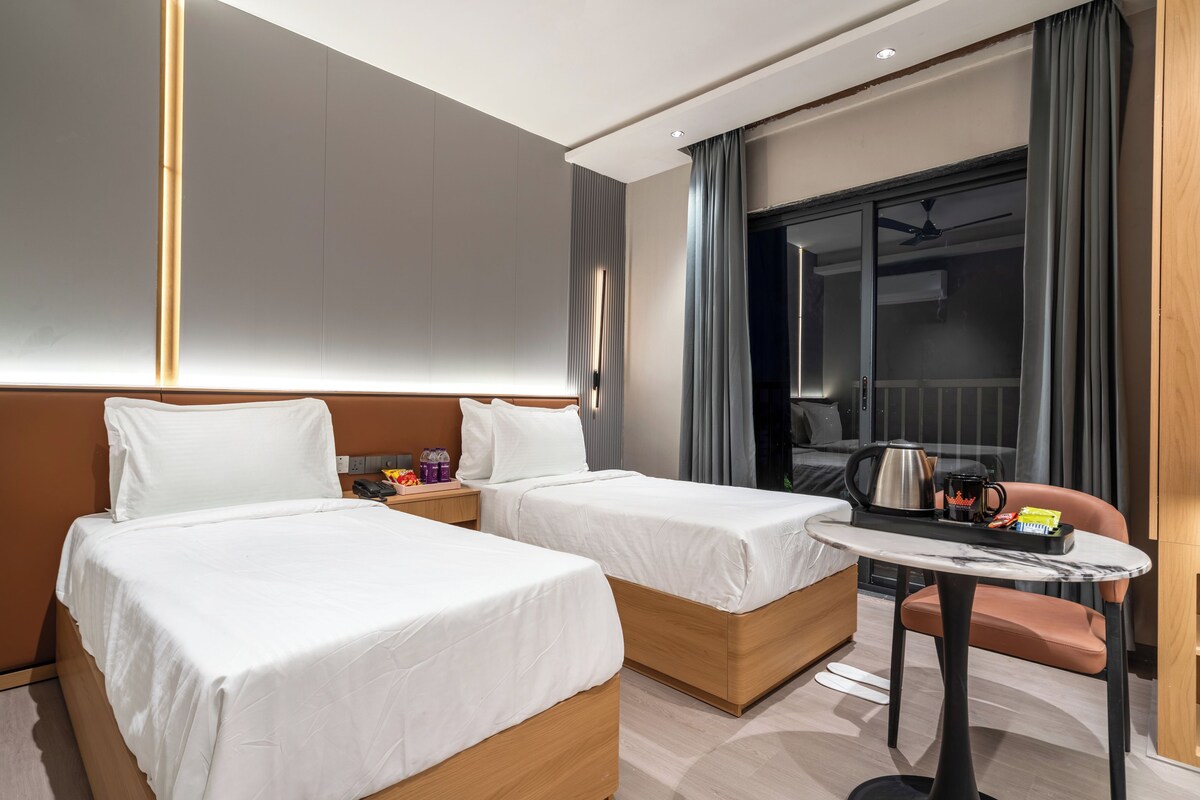 A hotel room with two beds, a small table, and a view of the outside.