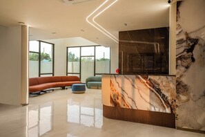 A modern interior with a marble reception desk, a curved bench, and large windows. - Triva By Rcc Hotels Financial District (Hyderabad)