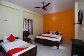Habitación de hotel con dos camas, ventilador de techo, televisor y ventana con cortinas.