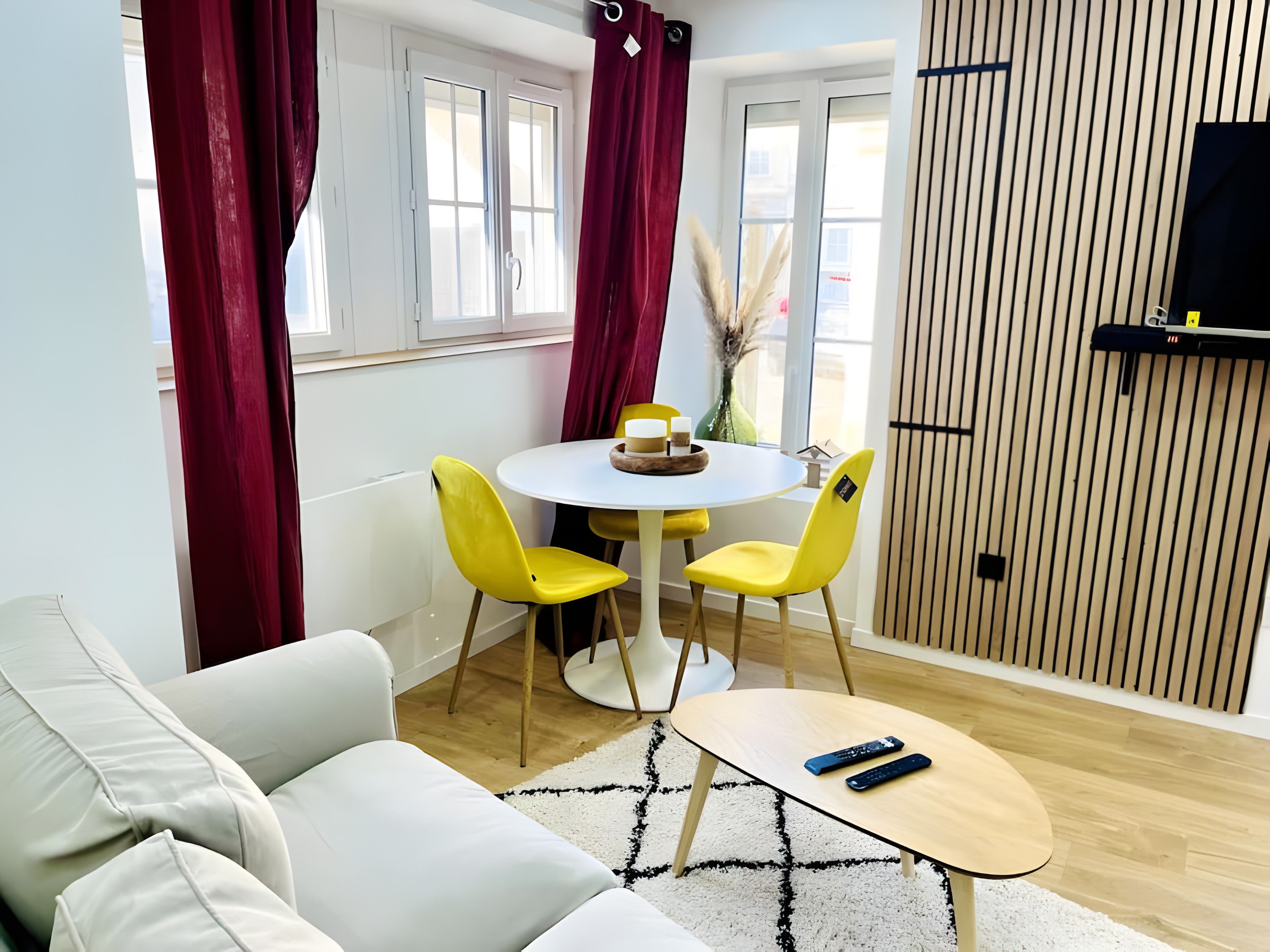 Ein modernes Wohnzimmer mit einem weißen Sofa, gelben Stühlen, einem runden Tisch und Holzböden.