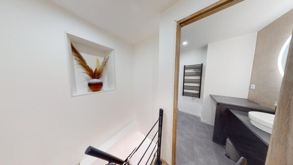 Un bagno moderno con una parete bianca, un porta asciugamani nero e un lavandino bianco.