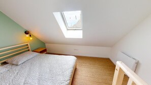 Una camera da letto con soffitto spiovente, un lucernario, un letto con copripiumino decorato, un comodino con una lampada e un termosifone.