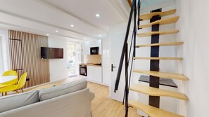 Un interno moderno con una scala, una zona pranzo con sedie gialle e una cucina con mobili bianchi.