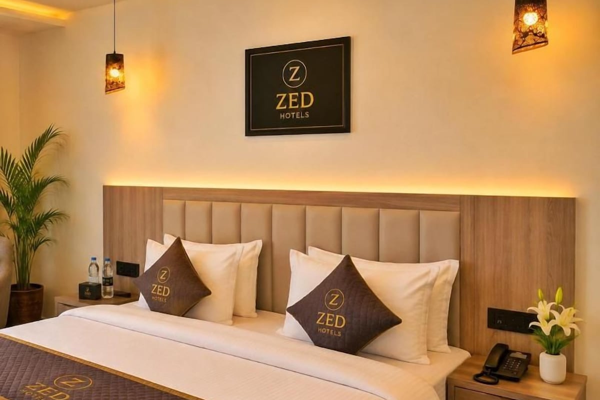 A hotel room with a bed, bedside tables, a nightstand, a lamp, and a framed sign on the wall.