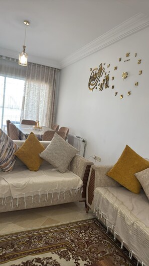 A living room with a sofa set, a dining table, and a decorative wall clock. - New Listing (Mahdia)
