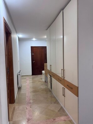 A hallway with a tiled floor, a radiator, a wooden door, and a wardrobe with multiple drawers. - New Listing (Mahdia)