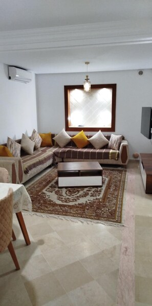 A living room with a sofa, a coffee table, a patterned rug, and a television. - New Listing (Mahdia)