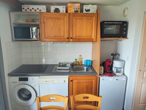 Een kleine keuken met houten kastjes, een magnetron, een broodrooster, een koffiezetapparaat en een wasmachine.