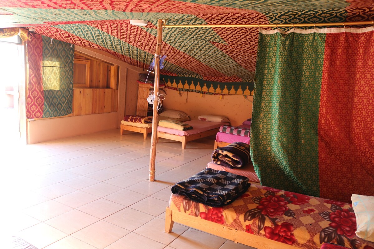 Ein Zimmer mit einem Bett, einem kleinen Tisch und einem Fenster mit Vorhängen.