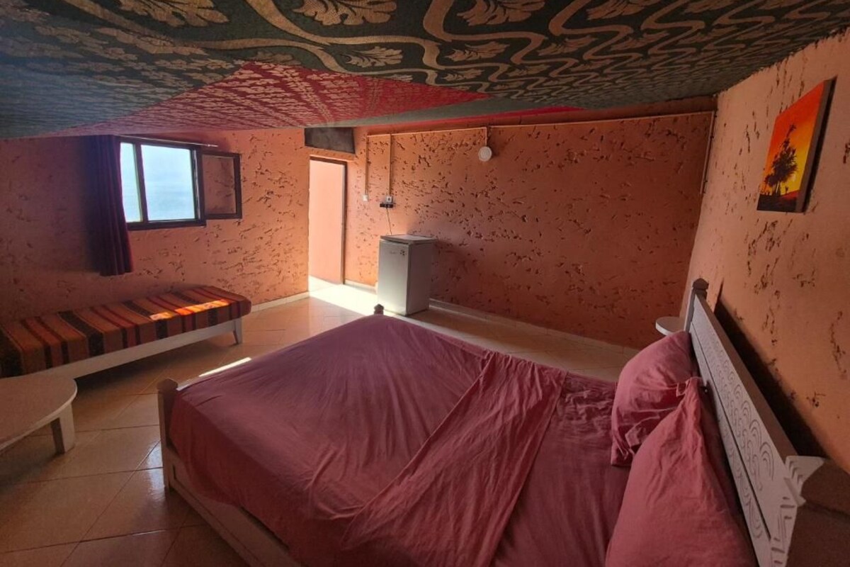 Ein Schlafzimmer mit einem Bett, einer Bank, einem kleinen Tisch, einem Fenster und einer Tür.
