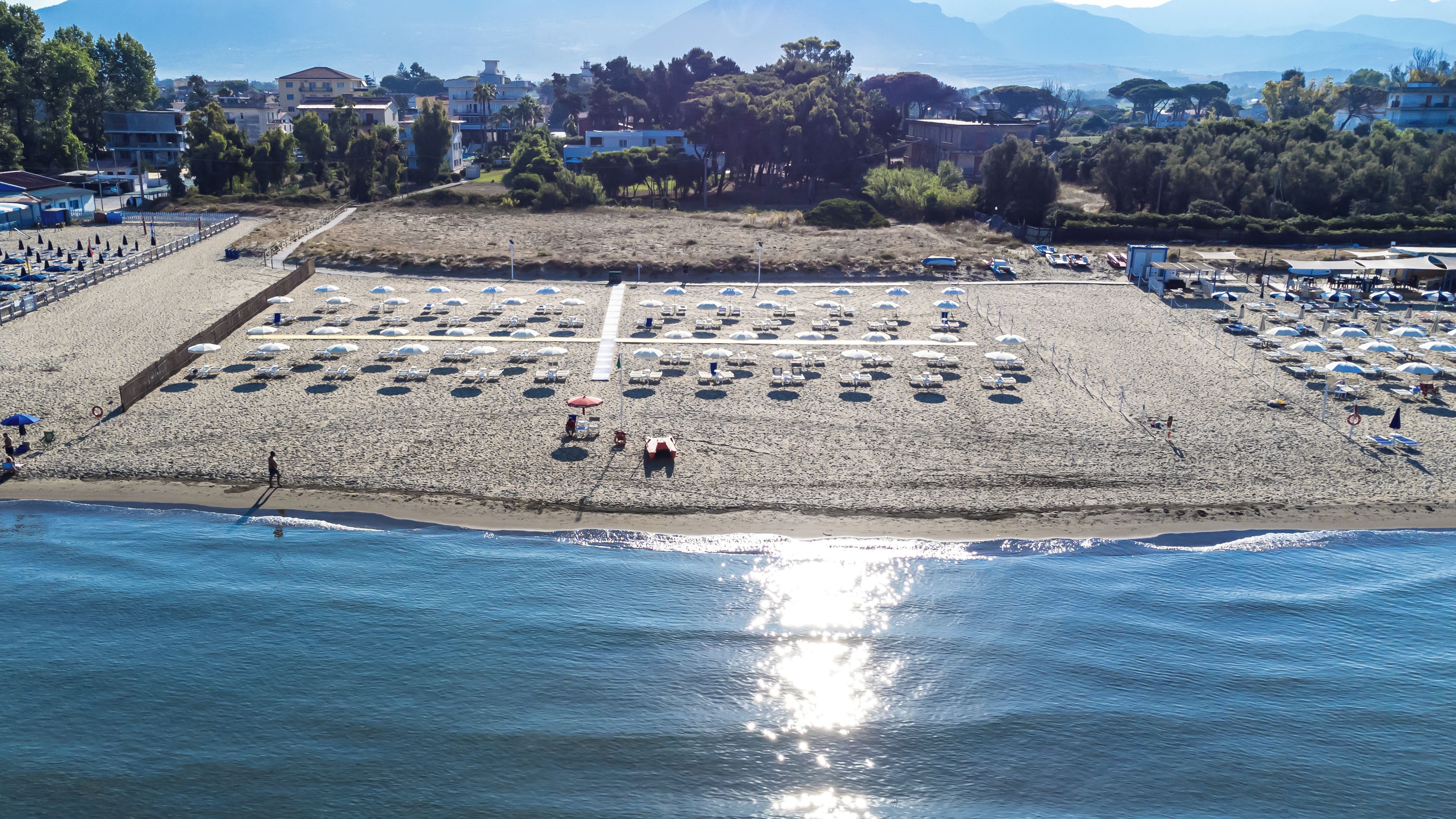 An aerial view of a beach with rows of umbrellas and sun loungers, a clear sky, and a calm sea.