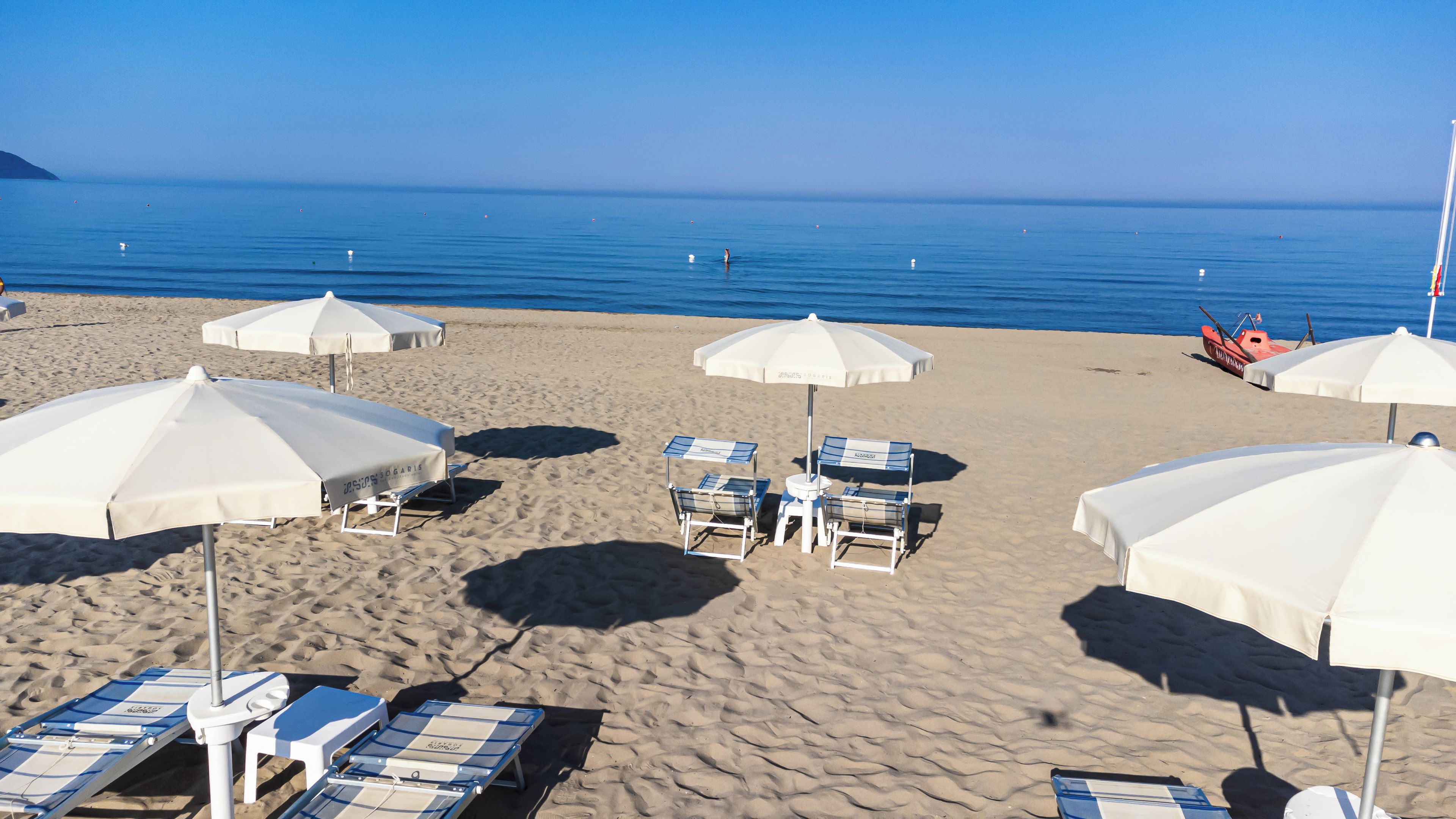 A beach with white umbrellas, lounge chairs, and a boat.