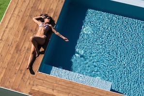 Una persona descansando sobre una terraza de madera junto a una piscina.