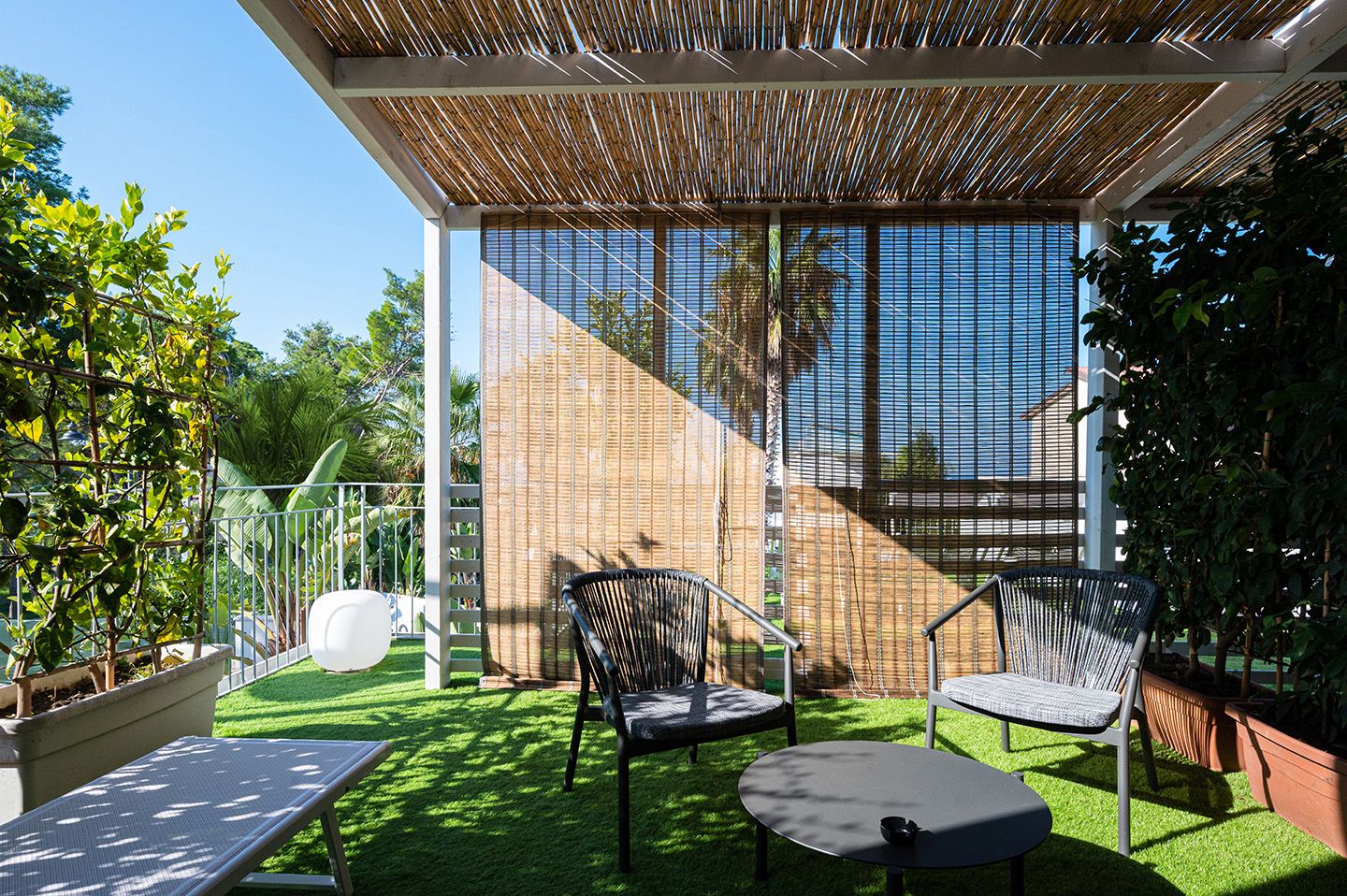 An outdoor patio with artificial grass, two wicker chairs, a round table, and a bamboo ceiling.