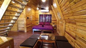 A wooden cabin with a sloped ceiling, a bed with purple bedding, a small table, and a bench. - Sapling's N Eyrie's Farm (Bhopal)