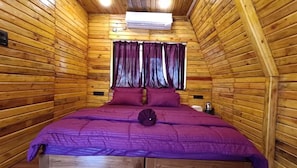 A wooden cabin room with a bed, purple bedding, and a window with curtains. - Sapling's N Eyrie's Farm (Bhopal)