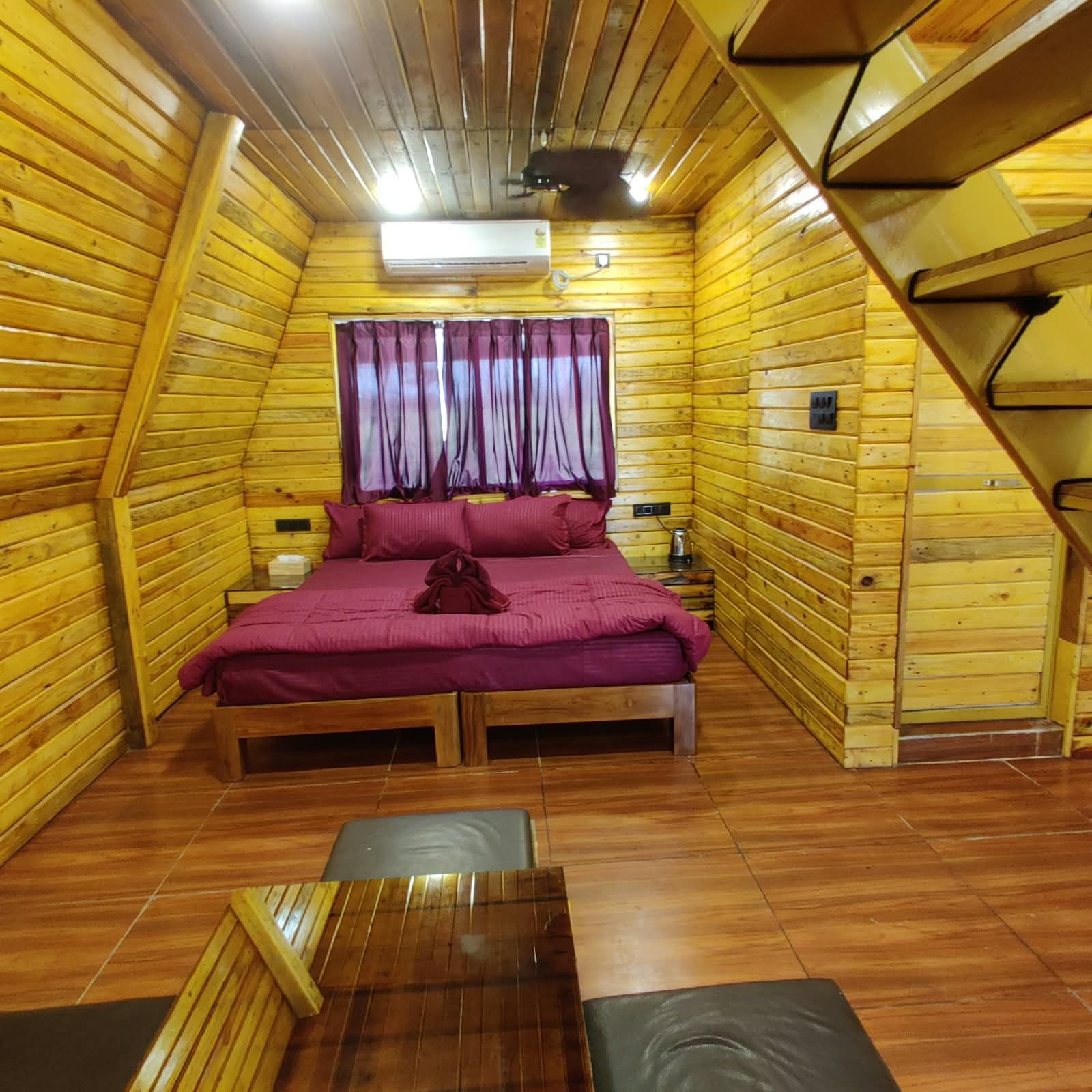 A wooden cabin room with a bed, a table, and a window with curtains.