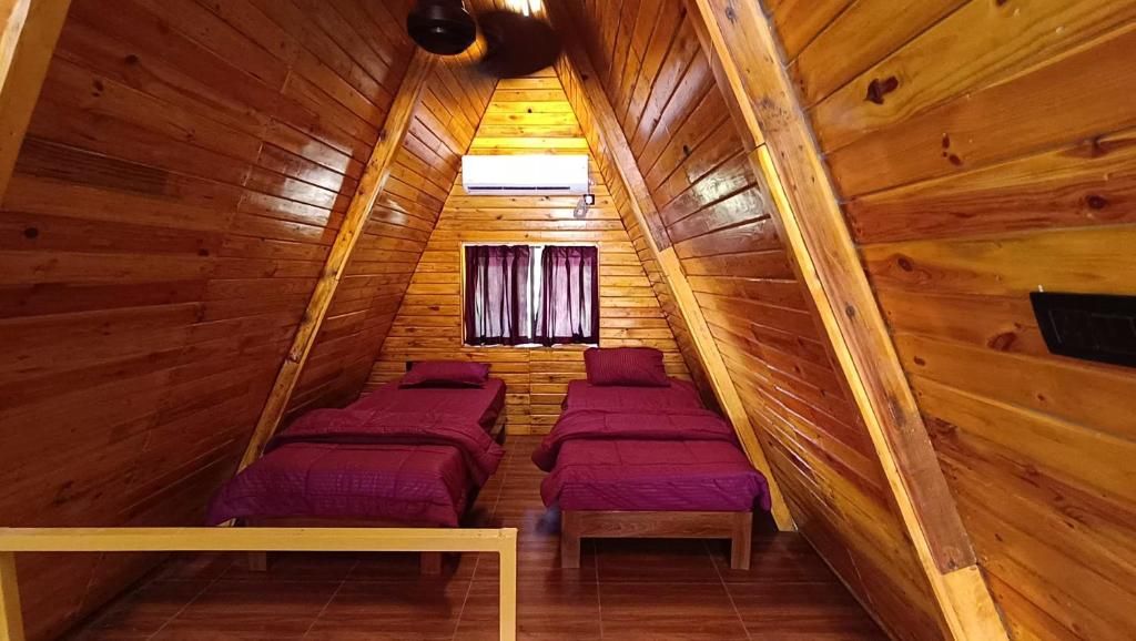 Eine Holzhütte mit geneigtem Dach, zwei Betten mit violetter Bettwäsche, einem Fenster mit Vorhängen und einem Deckenventilator.
