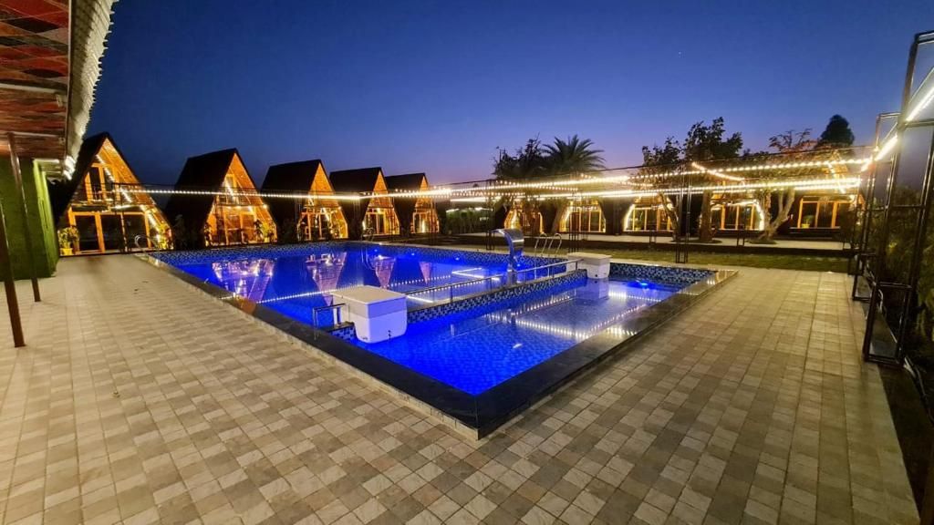 A swimming pool with a tiled deck, surrounded by buildings with warm lighting.