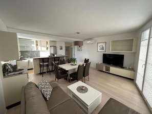 Ein moderner Wohnraum mit Essbereich, einer Couch, einem Fernseher und einer Küche im Hintergrund.