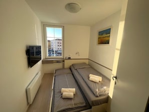 Ein kleines Hotelzimmer mit einem Bett, einem Fernseher, einem Fenster und einem Bild an der Wand.