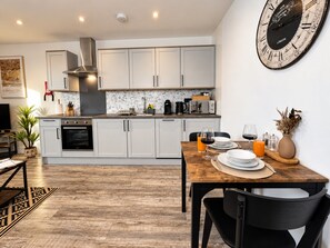 Une cuisine moderne avec des armoires blanches, un four encastré et un coin repas comprenant une table et des chaises en bois.