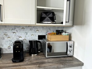 Une cuisine équipée d’une machine à café, d’une bouilloire, d’un grille-pain et d’un four à micro-ondes, le tout posé sur le plan de travail.