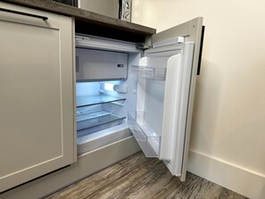 Vue intérieure d’une cuisine moderne équipée d’un réfrigérateur encastré, d’un four à micro-ondes et d’un évier en acier inoxydable.