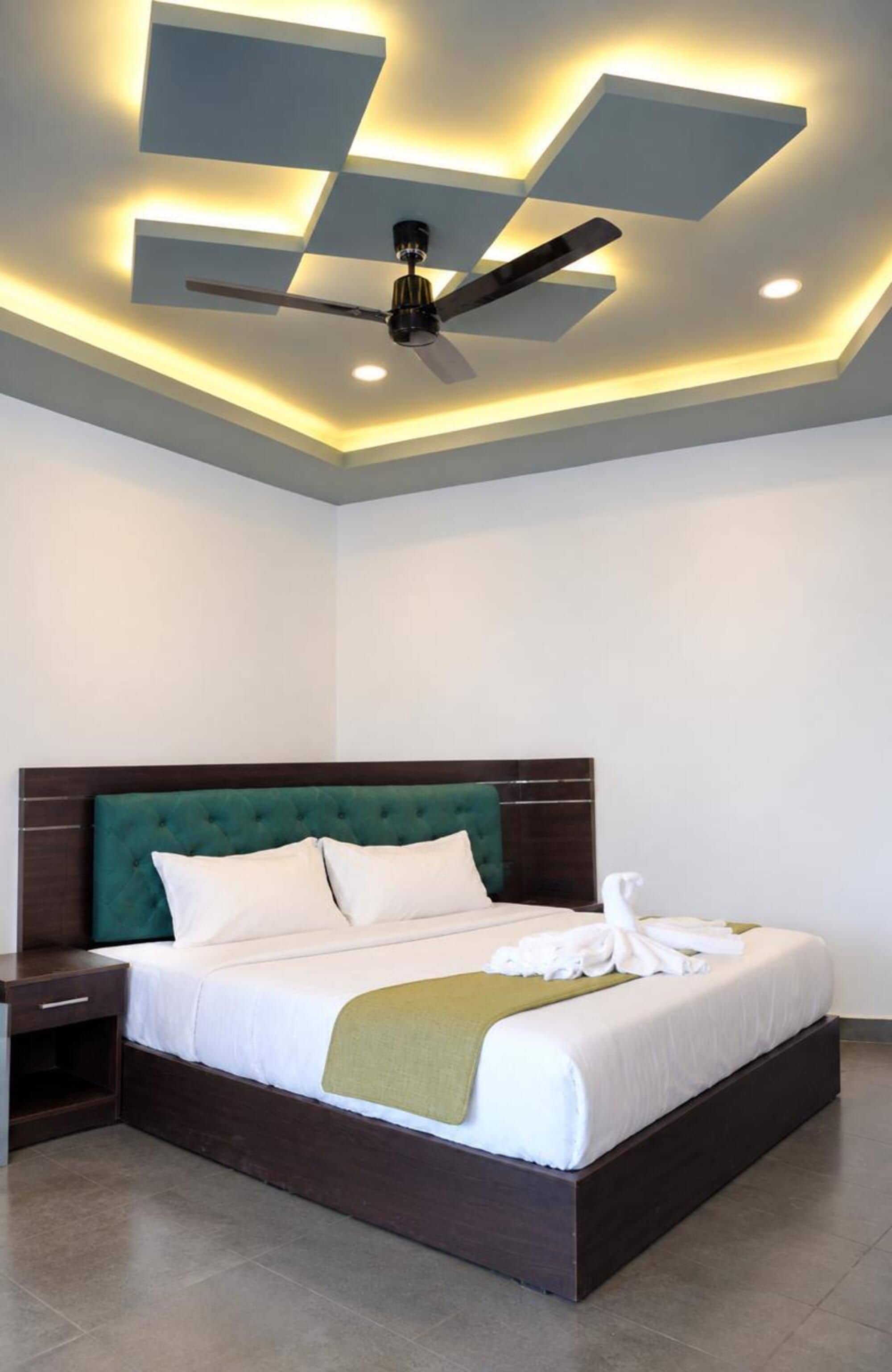Un dormitorio moderno con una cama grande, ventilador de techo, iluminación empotrada y una mesita de noche.