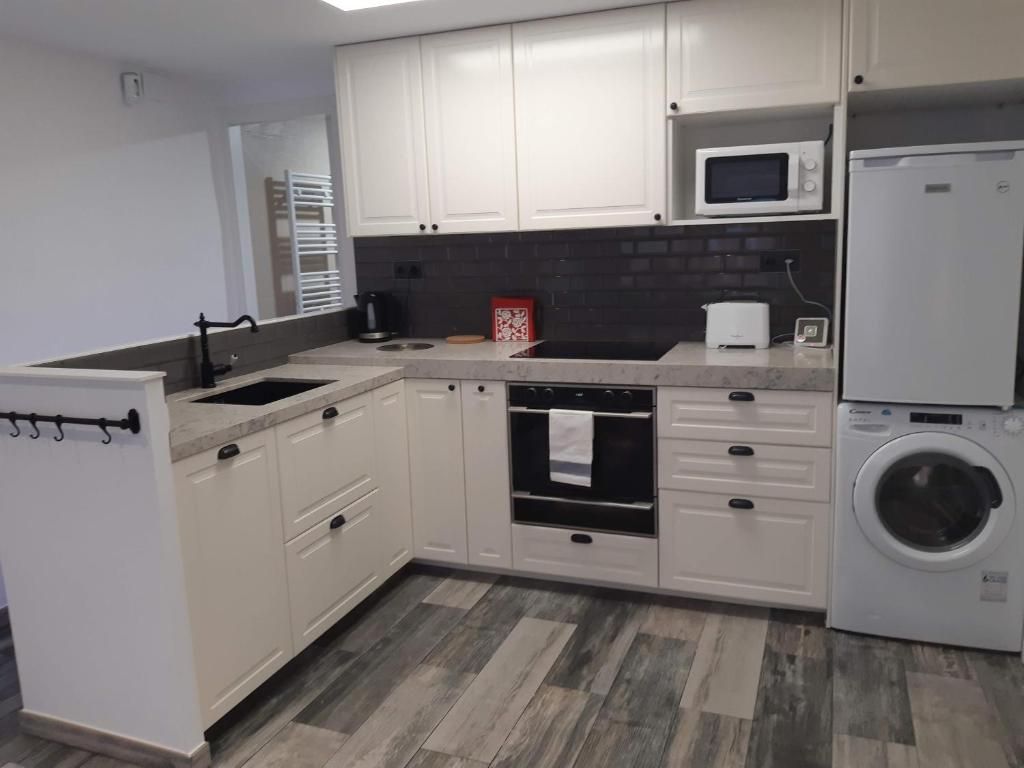 Una cocina con armarios blancos, microondas, lavadora y salpicadero de azulejos.