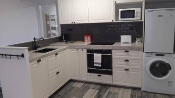 Una cocina con armarios blancos, microondas, lavadora y salpicadero de azulejos.