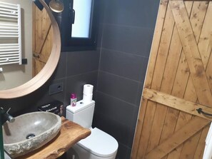 Un baño con tocador de madera, un lavabo redondo, un inodoro y una puerta de madera.