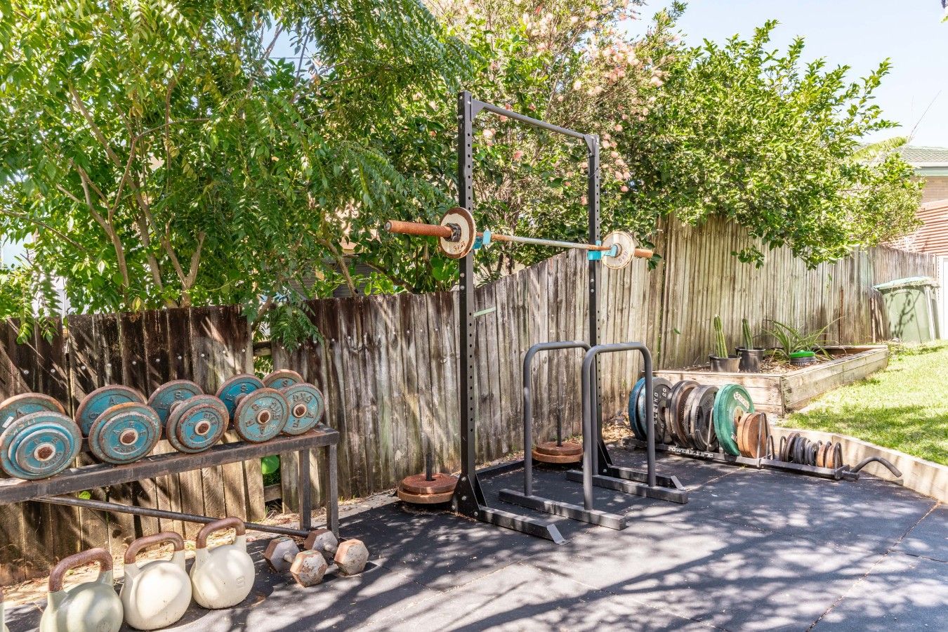 An outdoor gym with a pull-up bar, kettlebells, and weight plates.