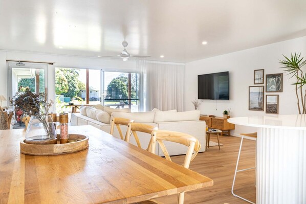 Un salon moderne avec une table à manger en bois, des canapés blancs et un téléviseur à écran plat fixé au mur.