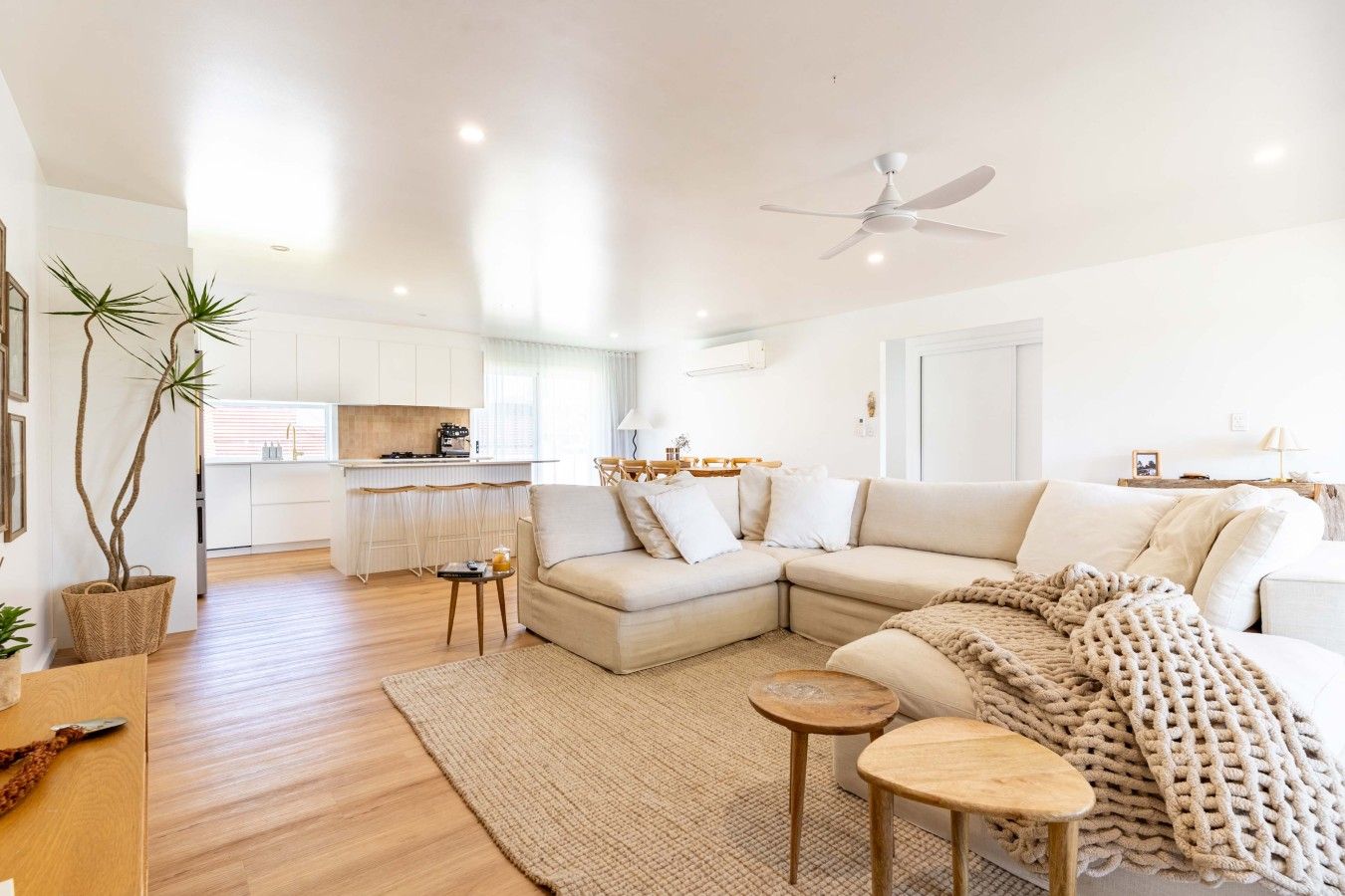 A modern living room with a sectional sofa, a coffee table, and a dining area with a kitchen in the background.