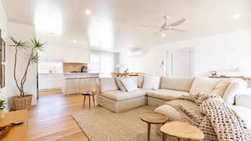 A modern living room with a sectional sofa, a coffee table, and a dining area with a kitchen in the background.