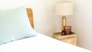 Un lit avec un oreiller bleu clair, une tête de lit en bois, une lampe de chevet et une petite table de chevet en bois sur laquelle se trouvent une bougie et une bouteille.