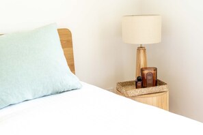 Un lit avec un oreiller bleu clair, une tête de lit en bois, une lampe de chevet et une petite table de chevet en bois sur laquelle se trouvent une bougie et une bouteille.