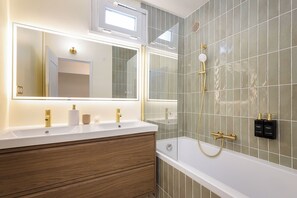 Een moderne badkamer met een wastafelmeubel met dubbele wastafel, een grote spiegel, een douche met handdouche en een bad.