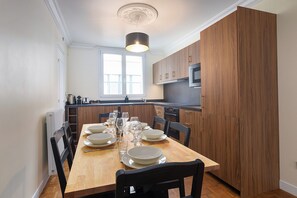 Een moderne keuken met houten kasten, een eettafel voor zes personen en een raam boven de gootsteen.
