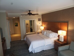 Ett hotellrum med en säng, två sänglampor, en takfläkt, en spegel och en dörr som leder till ett badrum.