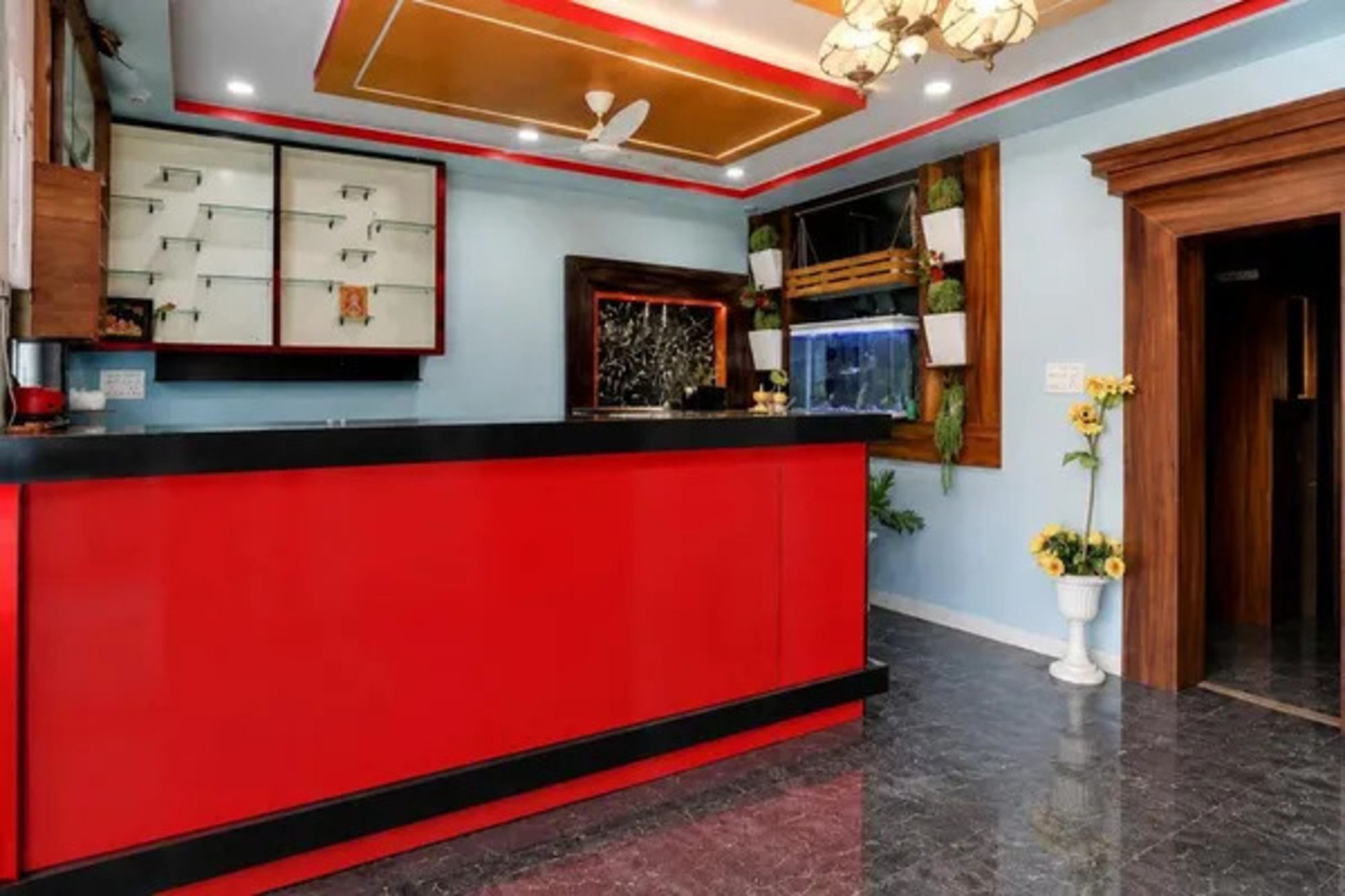 Un área de recepción con mostrador rojo, ventilador de techo y televisor montado en la pared.