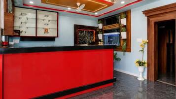Un área de recepción con mostrador rojo, ventilador de techo y televisor montado en la pared.