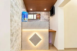 Un área de recepción con una pared de mármol, techo de madera y un televisor montado en la pared.