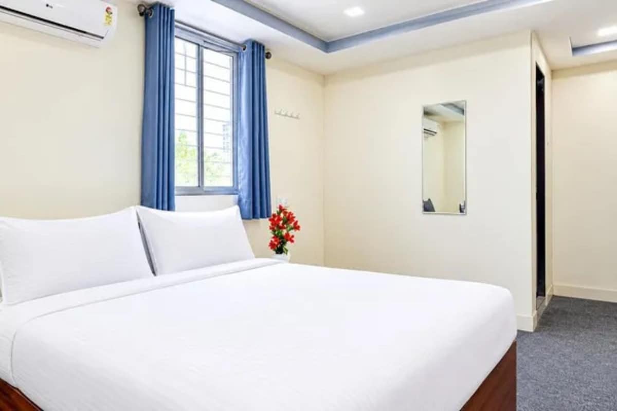 Una habitación de hotel con cama, ventana con cortinas, un espejo y un aire acondicionado instalado en la pared.