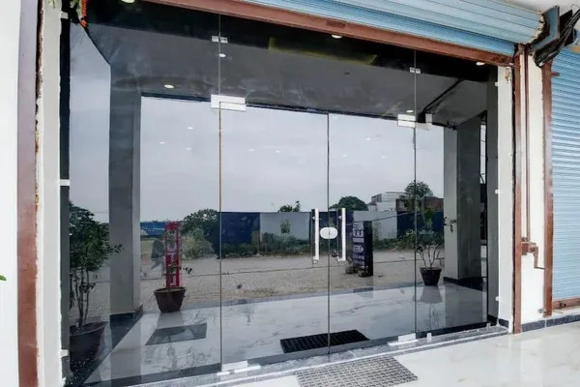 Entrada con puerta de cristal y marco metálico, una planta en maceta y un cartel en la pared.