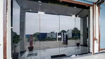 Entrada con puerta de cristal y marco metálico, una planta en maceta y un cartel en la pared.