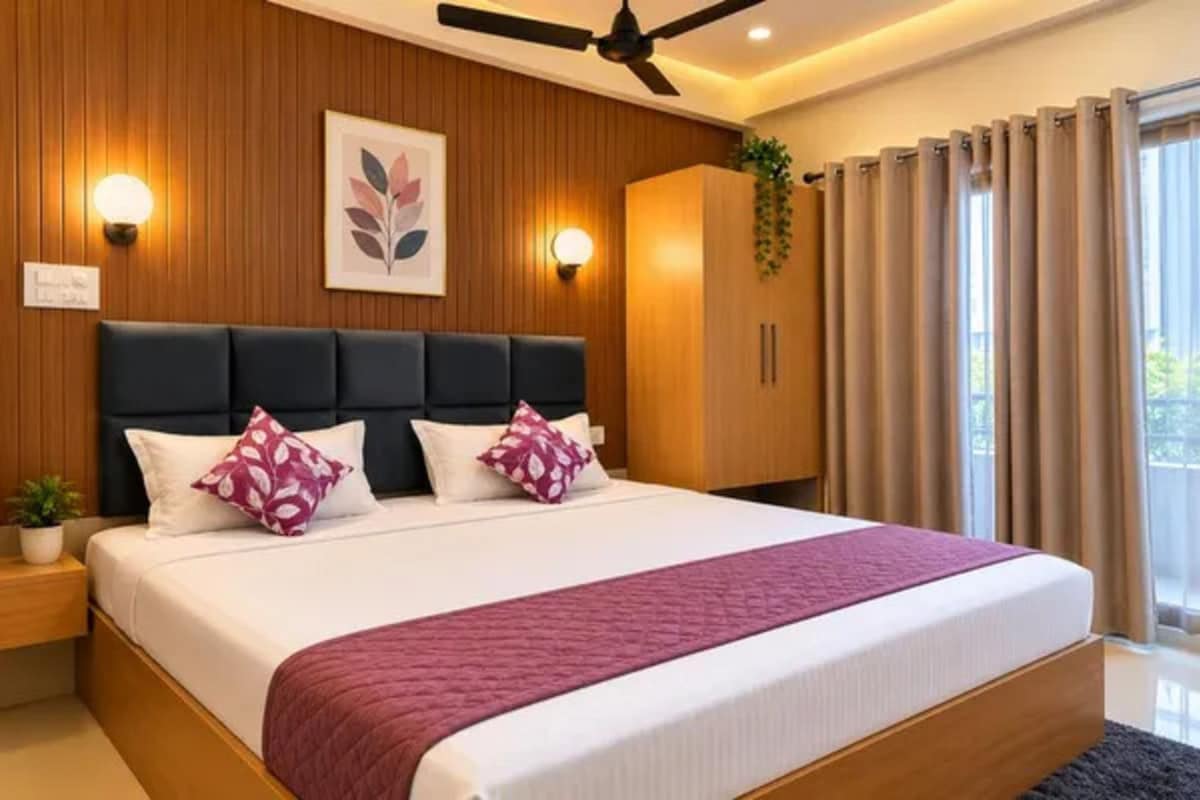 A modern bedroom with a large bed, wooden panel walls, a ceiling fan, and a view of the outdoors through curtains.